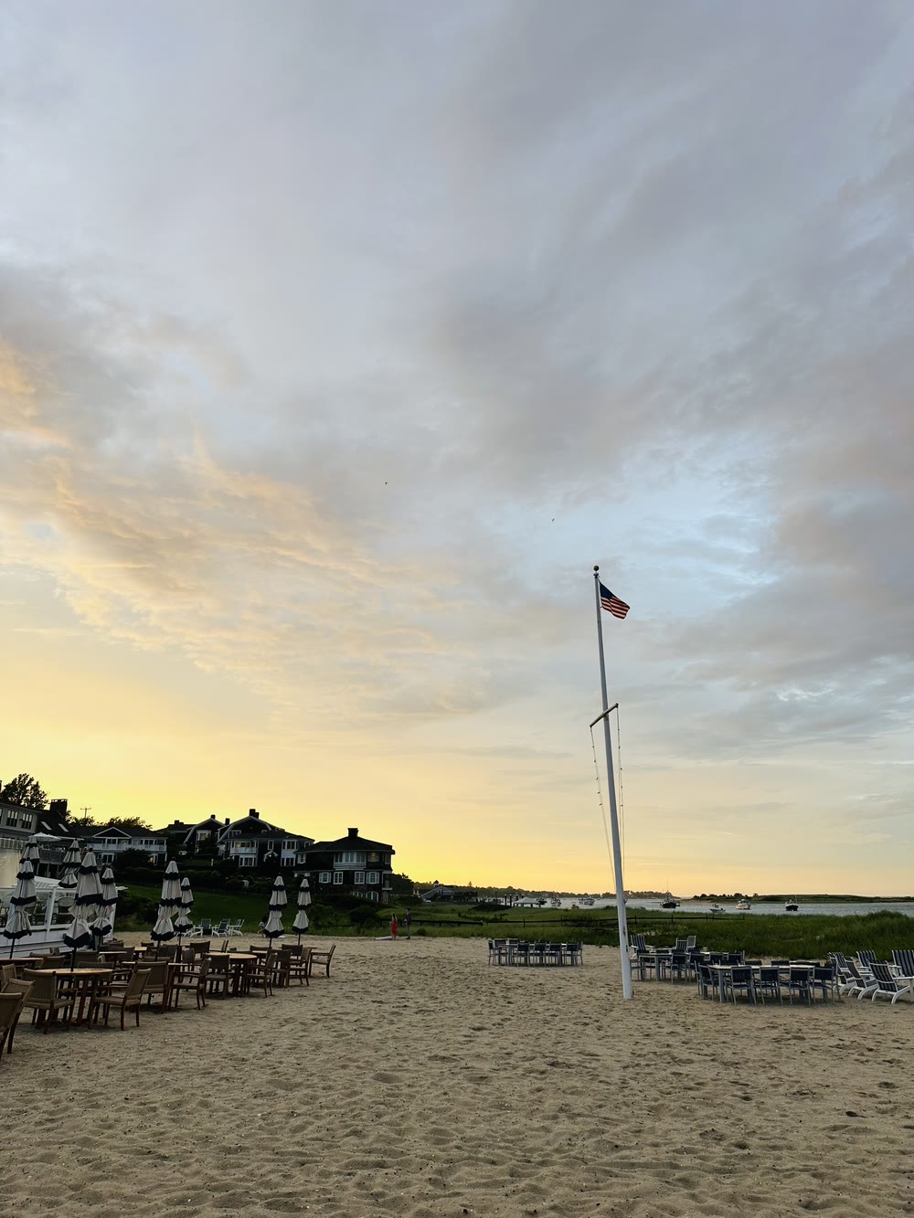 Sunset over the Chatham Bars Inn beach in Chatham, Massachusetts — Adirondack chairs, a flagpole and boats moored in the harbor under a golden sky